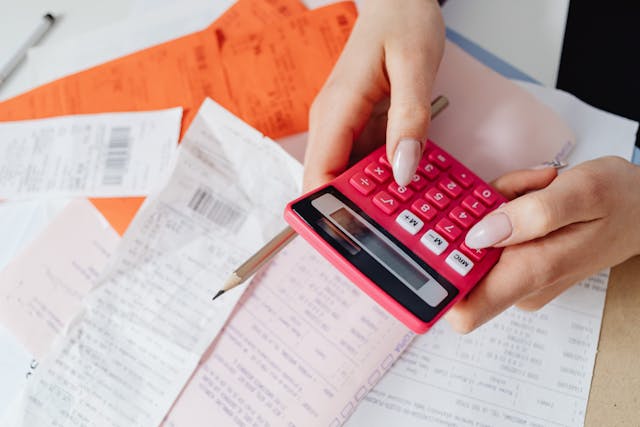 Person holding a calculator and a pen over top of a pile of receipts